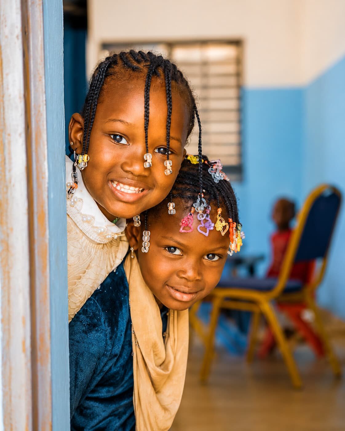 Deux sœurs nigériennes souriantes, tresses ornées de perles colorées, regard direct, symbole de la jeunesse que TAIMAKAB FOR HUMANITY accompagne