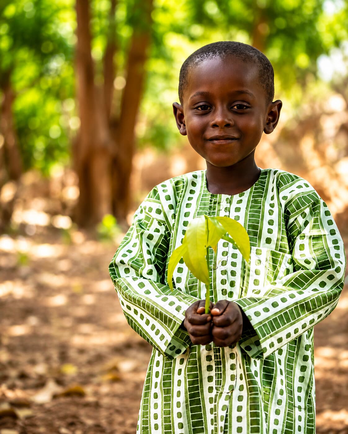 Jeune garçon nigérien en boubou vert traditionnel tenant une jeune plante